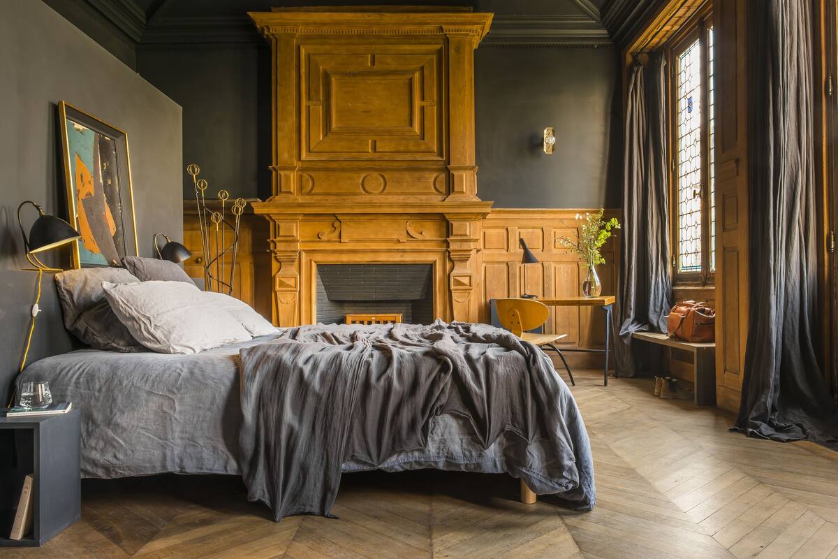 Ein Schlafzimmer mit einem großen Bett, einem Kamin aus Holz, einem Schreibtisch mit Stuhl und einem Fenster mit Vorhängen.