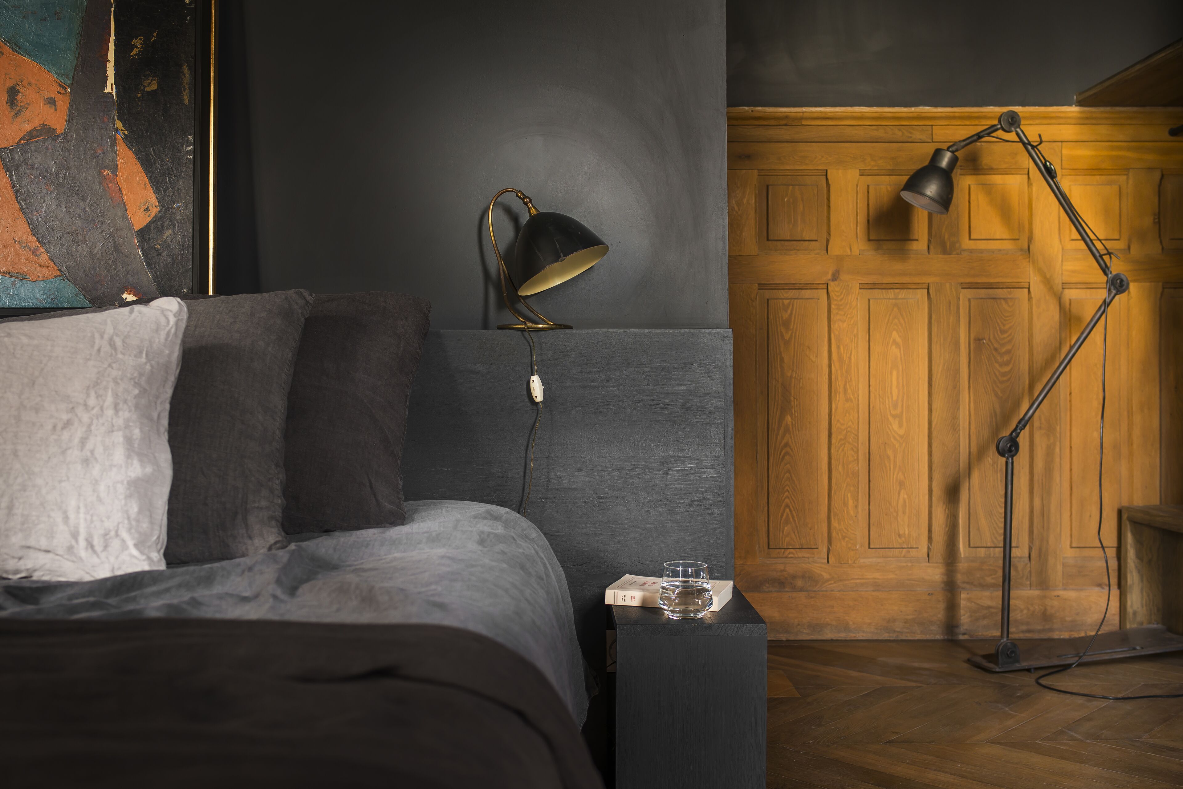 Une chambre à coucher avec un lit, une table de chevet, une lampe de bureau et une porte en bois.