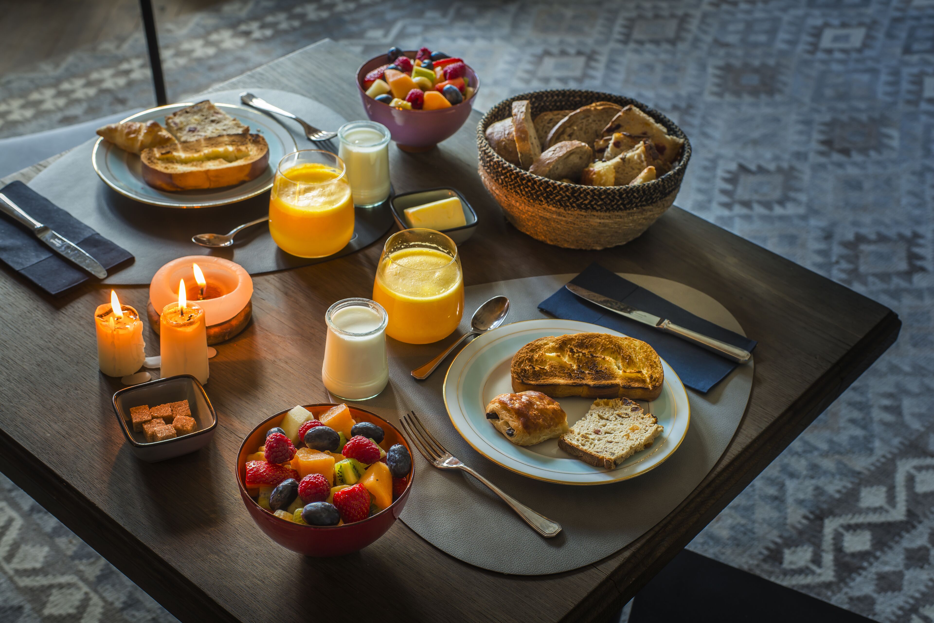 A breakfast table with toast, fruit, juice, and a bowl of cereal.