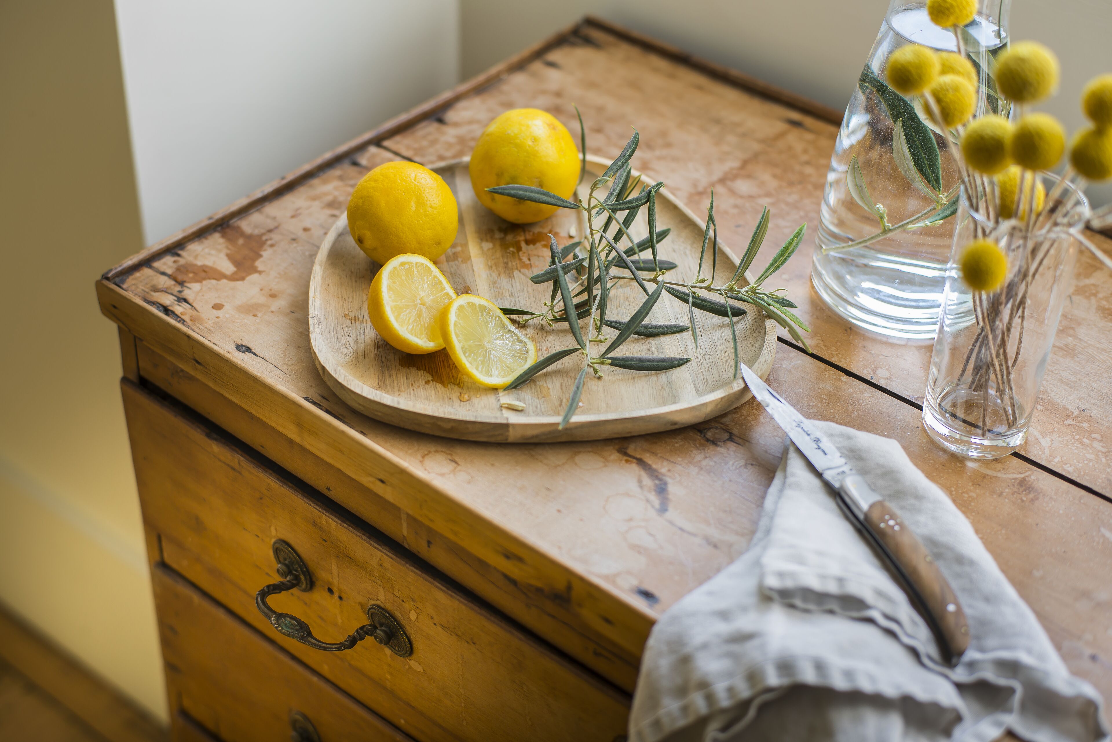 Una mesa de madera con tabla de cortar, limones, romero y un cuchillo.