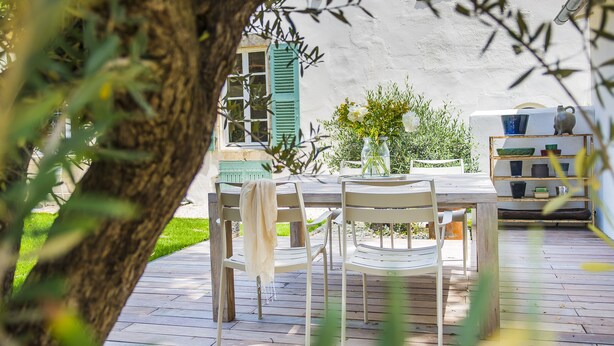 An outdoor patio with a wooden table and chairs, surrounded by greenery and a white wall. - Le Secret (Saint-Martin-de-Re)