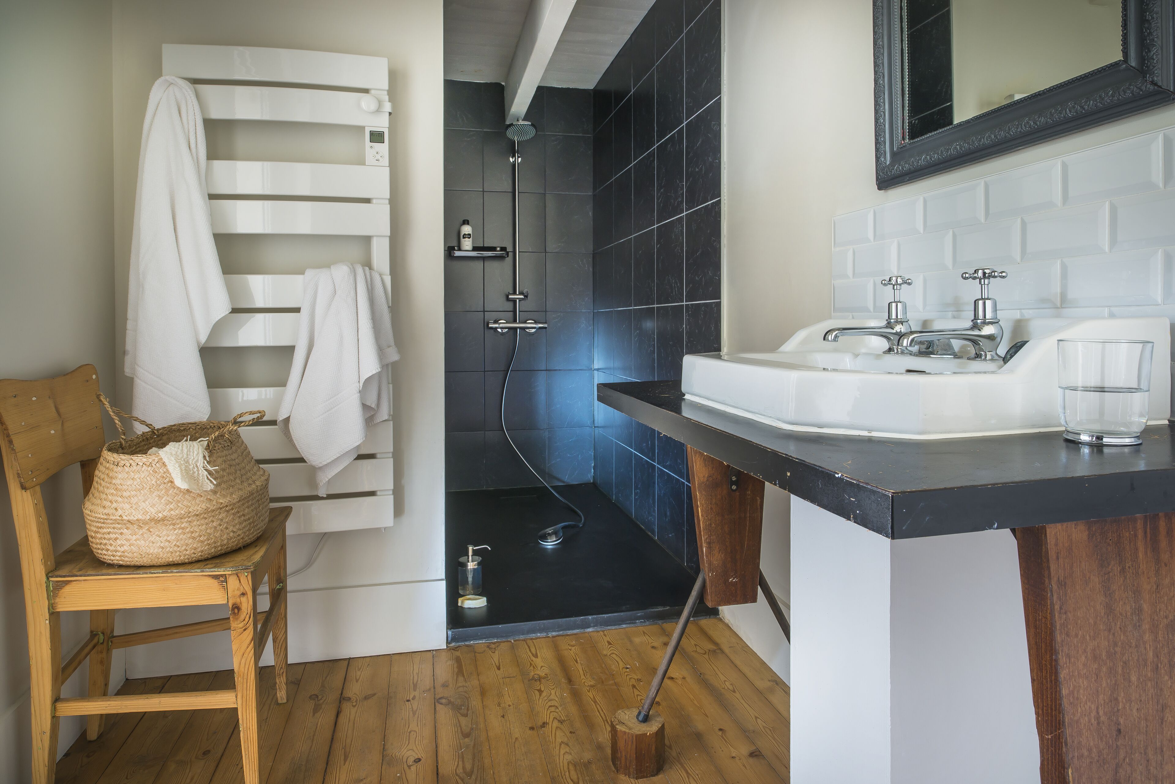 A modern bathroom with a shower, a sink, and a wooden chair with a woven bag.