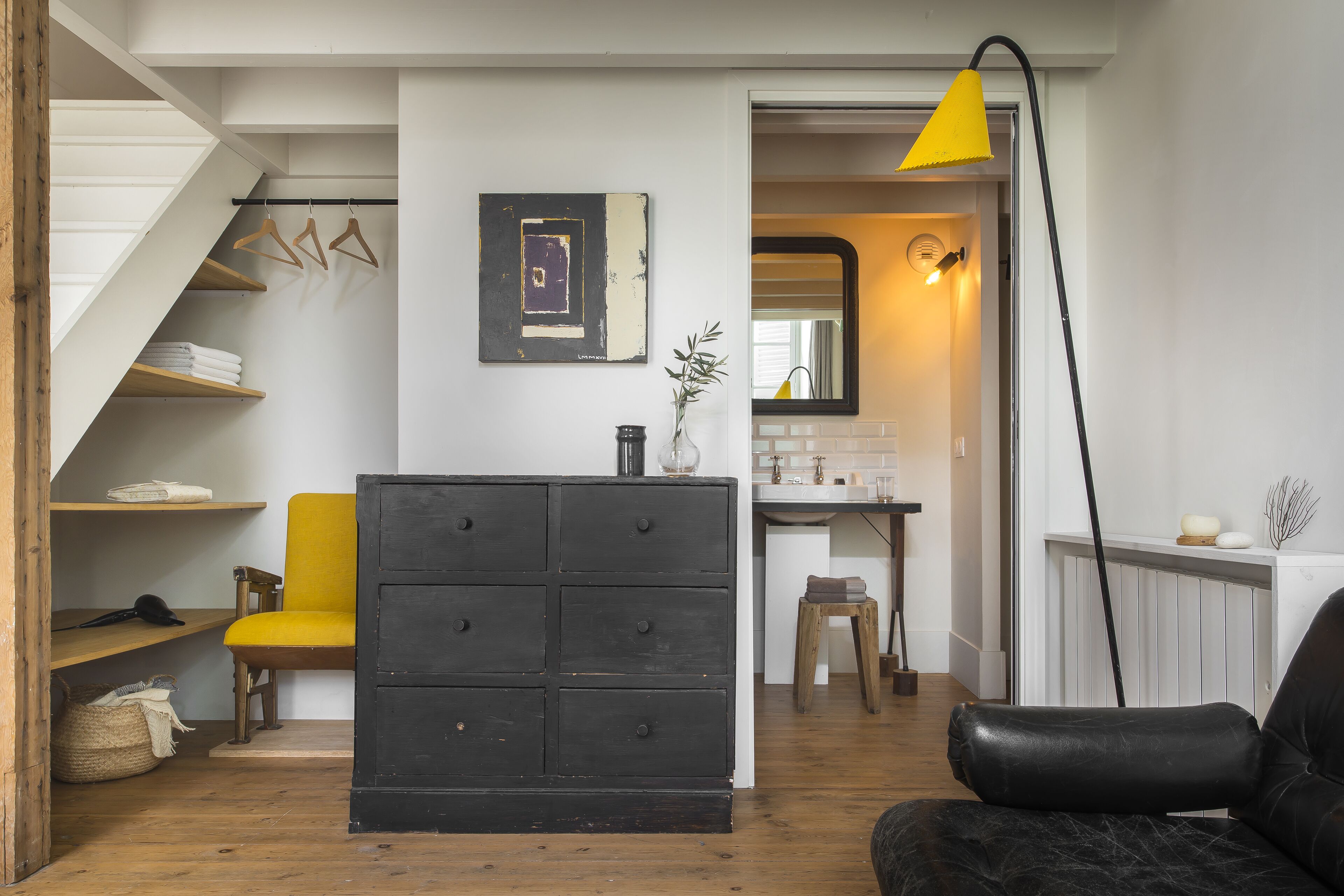 A room with a staircase, a black chest of drawers, a yellow chair, and a black sofa.