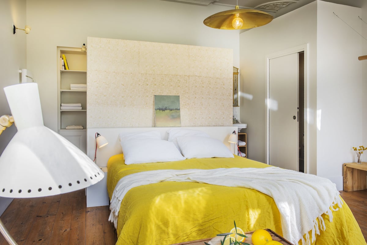 Ein Schlafzimmer mit Bett, Nachttischen, einer Lampe, einem Regal mit Büchern und einer Tür.
