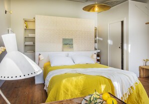 Un dormitorio con cama, mesitas de noche, lámpara, estantería con libros y una puerta.