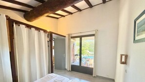 Quarto com cama, cortinas, porta e vista para área externa.
