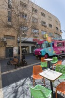 Un camión de comida colorido estacionado frente a un edificio con un letrero que dice "GOLF". Hay zonas de estar al aire libre con sillas verdes y naranjas.