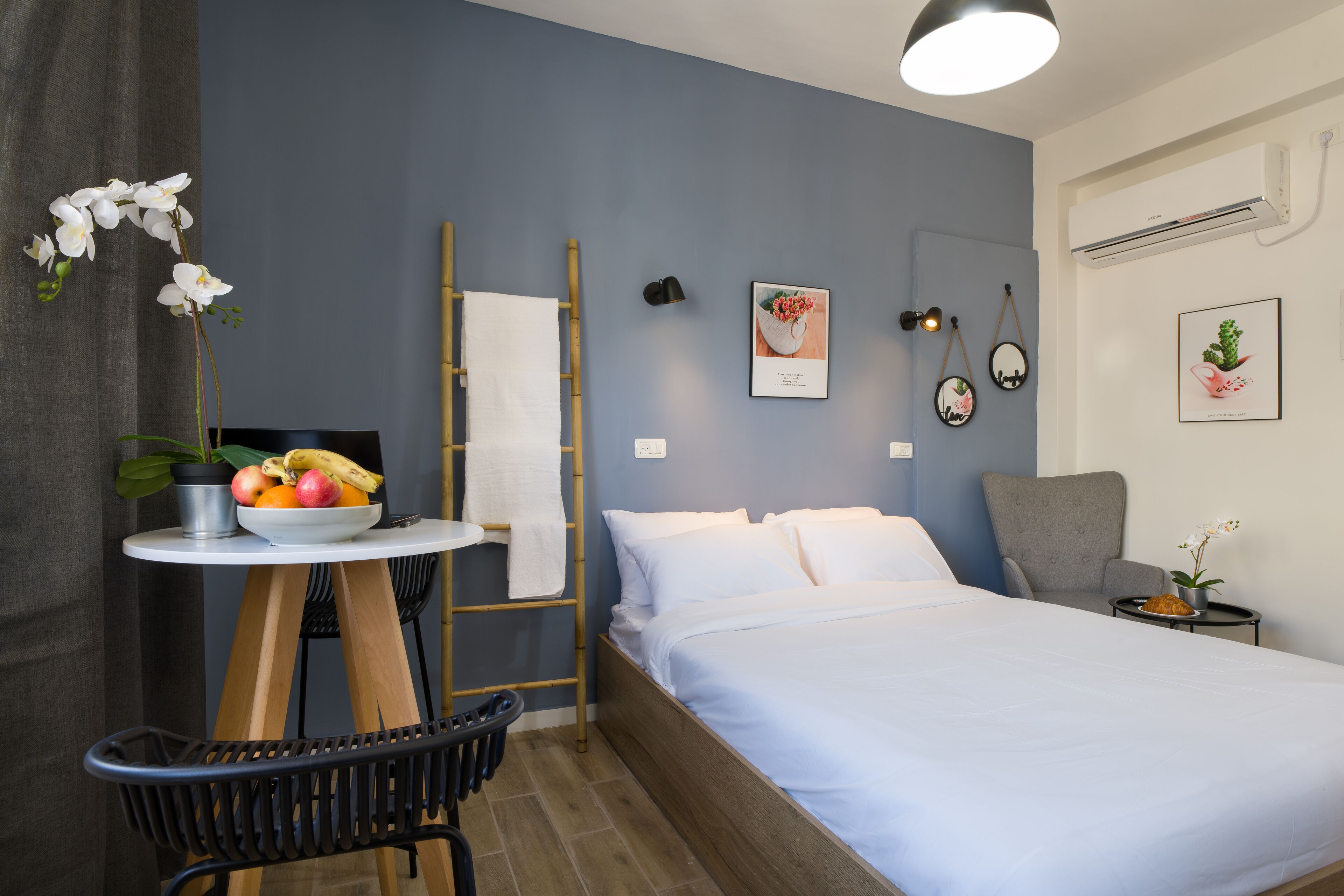 Un dormitorio con una cama, una mesita con fruta, una silla, una escalera y un aire acondicionado instalado en la pared.