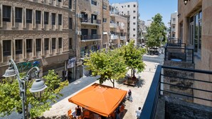 A multi-story building with balconies, outdoor seating, and a tree in the foreground. - Aju Ben Yehuda 23 (Jerusalem)