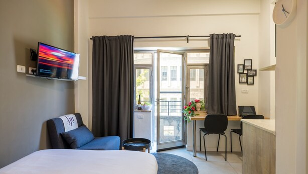 A hotel room with a bed, a desk, a chair, a TV, and a balcony with curtains. - Aju Ben Yehuda 23 (Jerusalem)