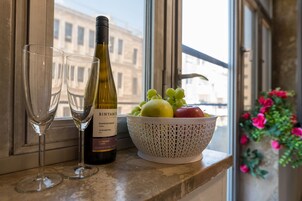Una botella de vino, dos copas y un bol de fruta sobre un alféizar.