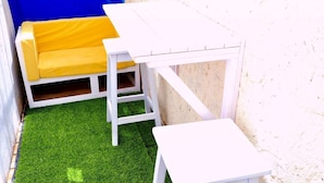Un pequeño espacio al aire libre con una mesa blanca y un banco amarillo acolchado.