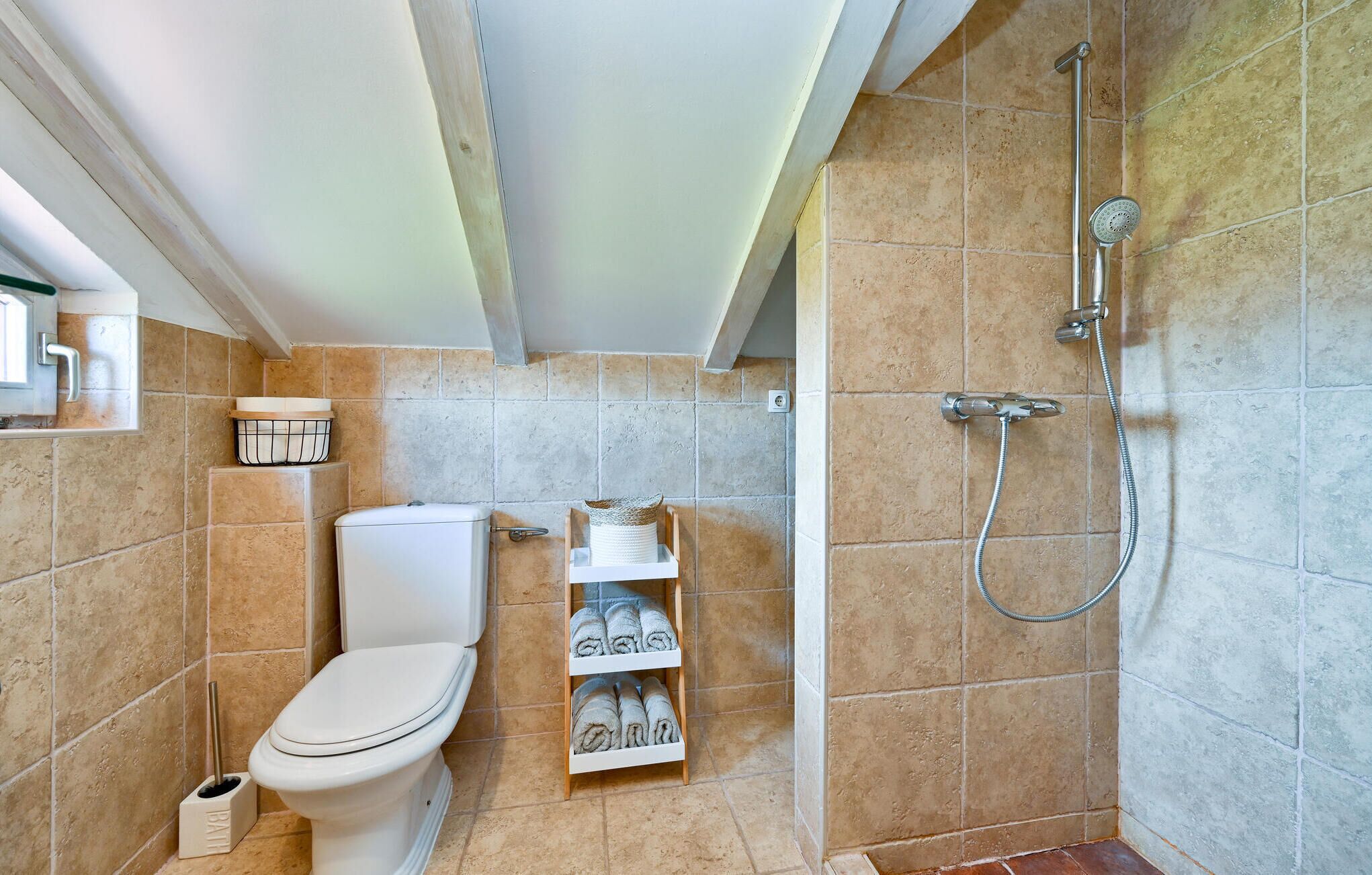A bathroom with a toilet, a shelf with towels, and a shower area.