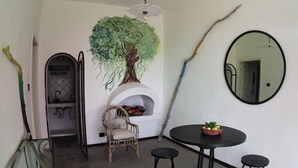 Un comedor con una mesa redonda, cuatro taburetes, una silla de mimbre, un espejo en la pared y un cuadro de un árbol.