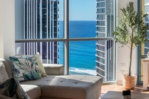A living room with a large window offering a view of the ocean and high-rise buildings.