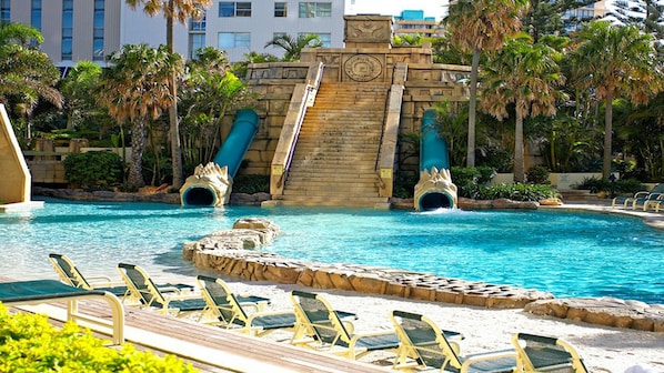 A swimming pool with slides, lounge chairs, and palm trees.