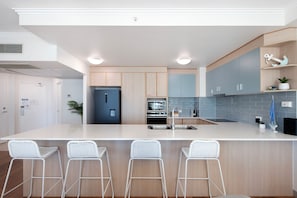 A modern kitchen with a central island, bar stools, and a built-in oven.