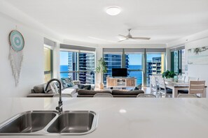 A modern kitchen with a dining area, large windows, and a view of the ocean.