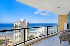 En balkon med udsigt over stranden og havet, med en høj bygning i baggrunden.