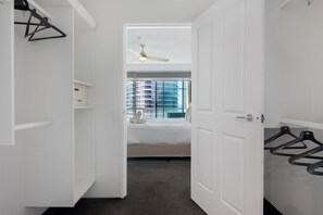 A hotel room with a bed, a ceiling fan, a window with a view of buildings, and a door with a coat rack.