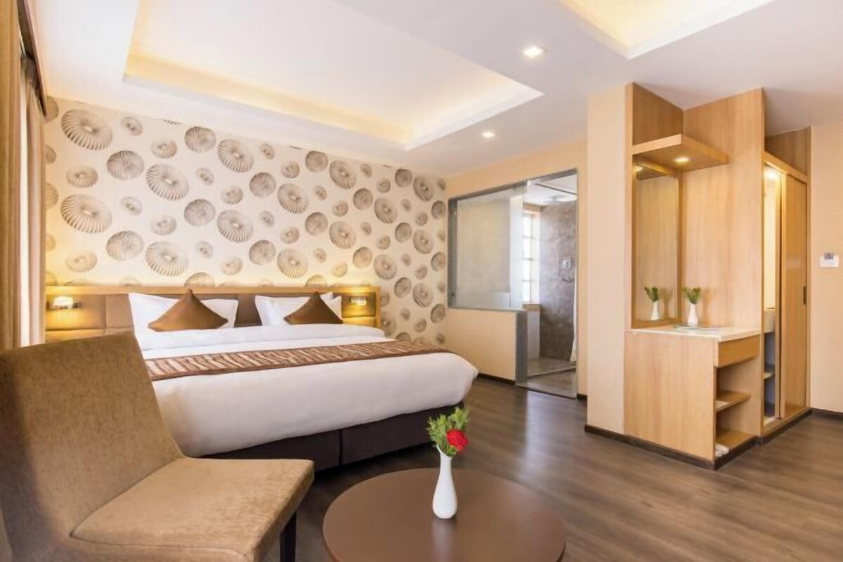 Une chambre d’hôtel avec un lit, un canapé, une petite table avec un vase, une armoire et un miroir.