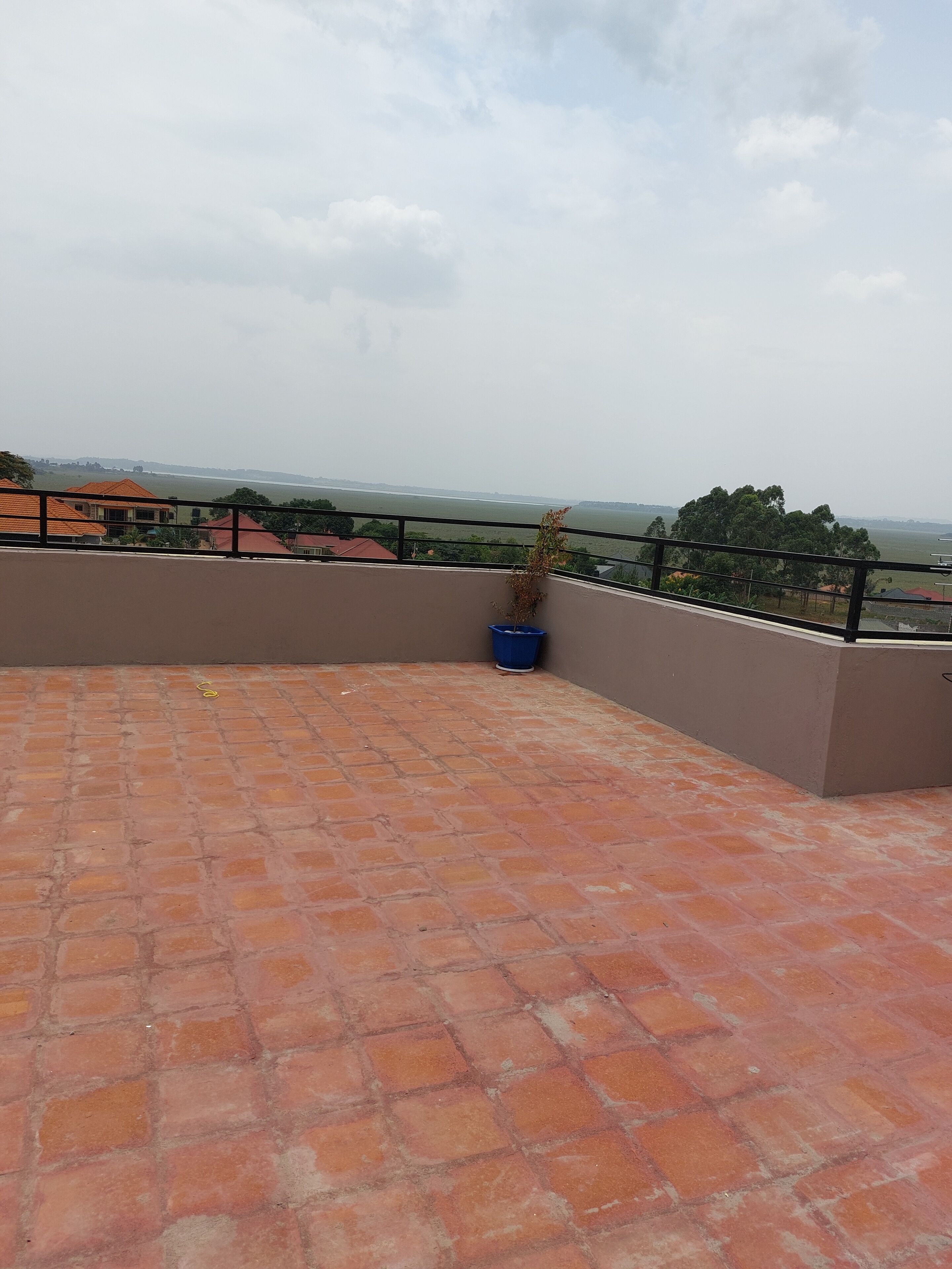 A rooftop terrace with a brick floor, a blue trash bin, and a view of a distant landscape.