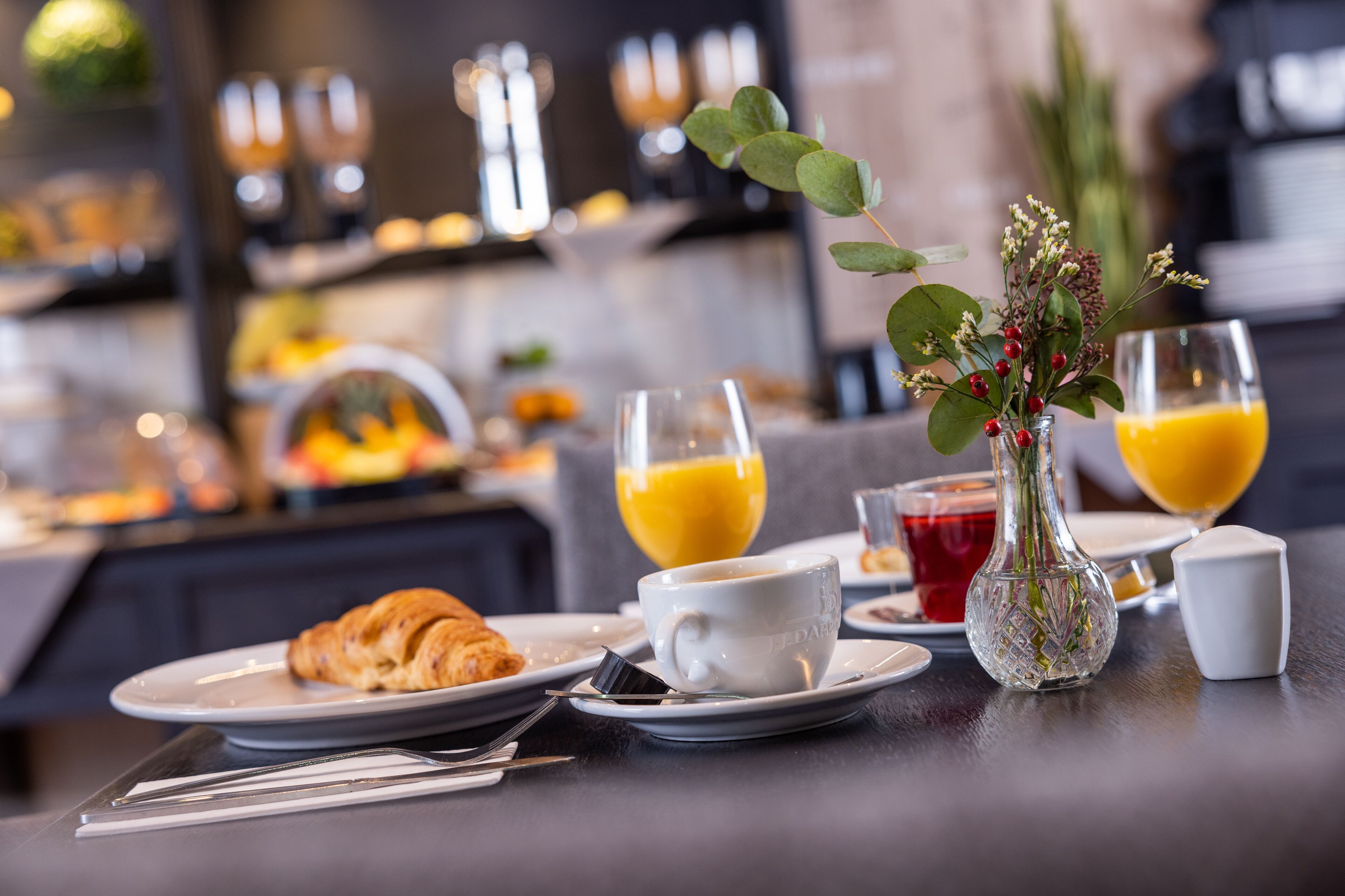 Una escena de desayuno con cruasanes, tazas de café y vasos de jugo de naranja sobre una mesa.
