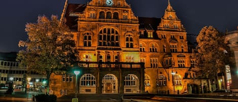 Un edificio histórico con una destacada torre de reloj, grandes ventanales de arco y una fachada simétrica.