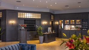 A reception area with a dark wood reception desk, a large potted plant, and a blue upholstered chair. - Ravensberger Hof (Bielefeld)