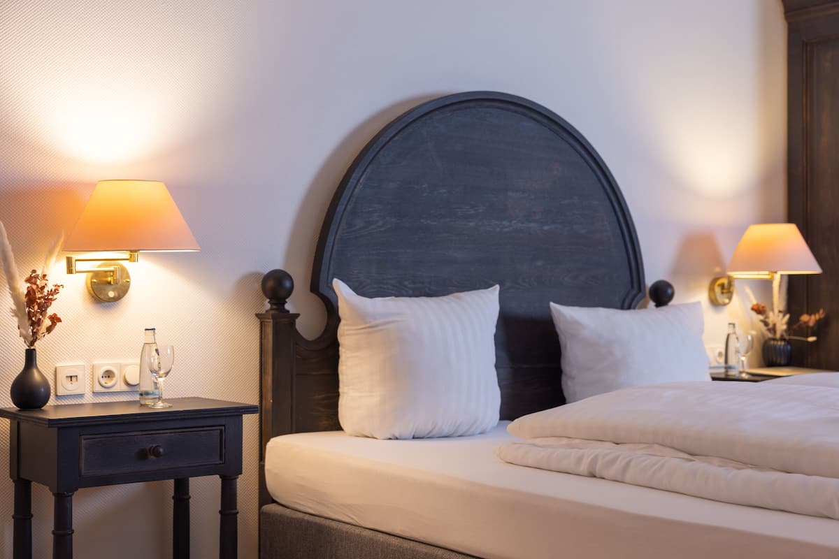A neatly made bed with white bedding, a dark wooden headboard, and two bedside lamps with lampshades.