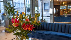 A modern interior with a blue sofa, a glass table with a flower arrangement, and large windows offering a view of the city. - Ravensberger Hof (Bielefeld)