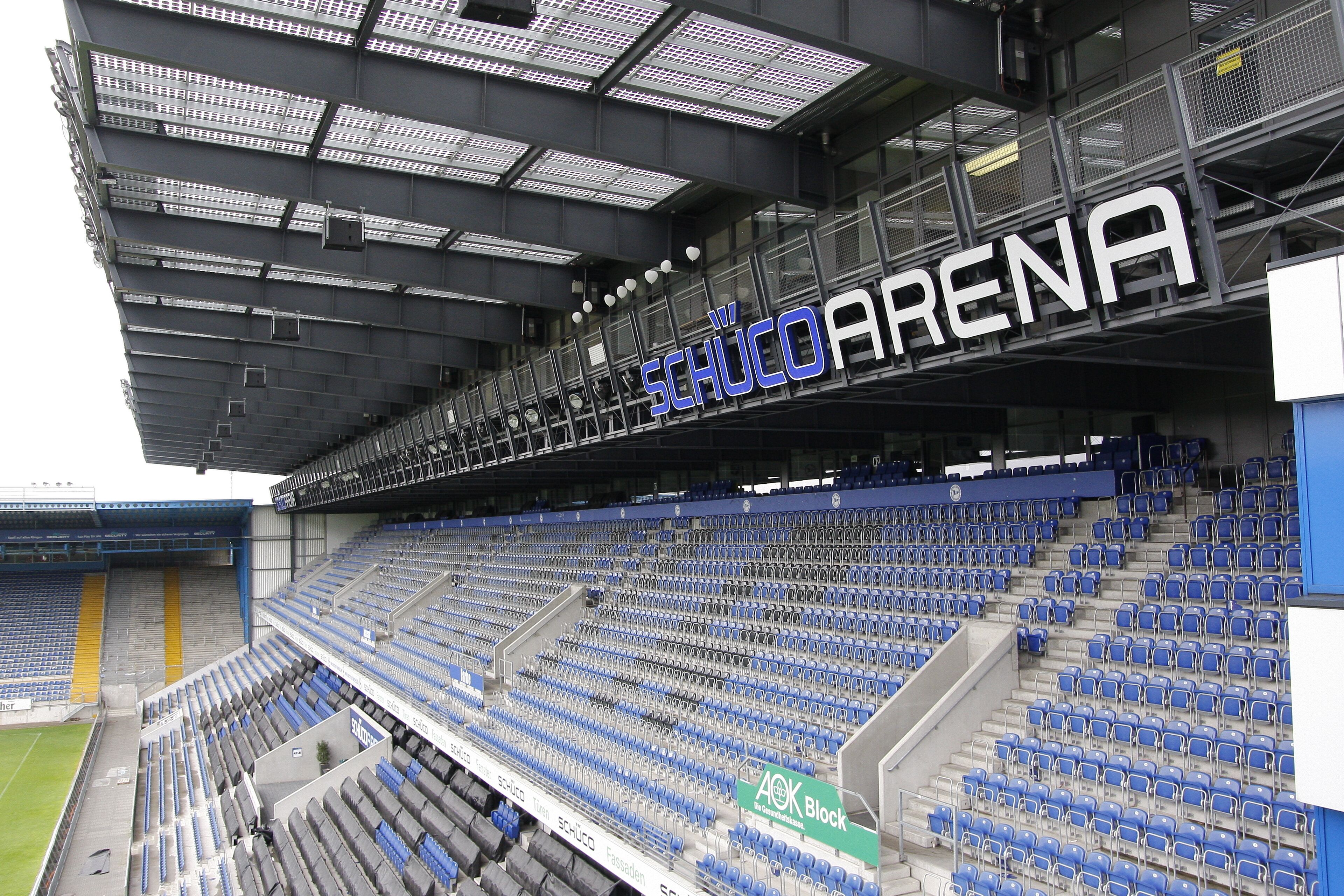 Un estadio vacío con asientos azules y un letrero grande que dice "SCHUCO ARENA".