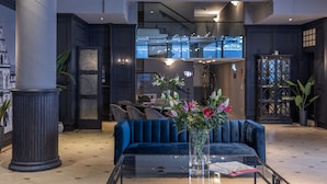 A modern lobby with a blue sofa, a glass coffee table, and a vase with flowers. - Ravensberger Hof (Bielefeld)