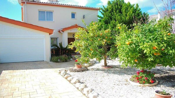 A house with a garage, a driveway, and a garden with trees and potted plants.