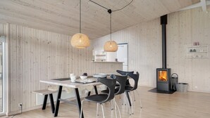 Ein modernes Interieur mit einer Holzwand, einem Esstisch mit Stühlen, einer Pendelleuchte und einem Kaminofen.