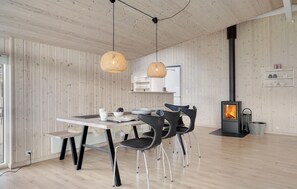 A modern interior with a wooden wall, a dining table with chairs, a hanging light fixture, and a wood-burning stove. - Amazing home in Løkken with sauna (Løkken)