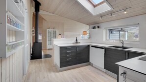 Eine moderne Küche mit Oberlicht, Holzböden und einer zentralen Kochinsel mit Spüle und Weingläsern.