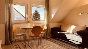 Um quarto aconchegante com uma mesa de jantar, duas cadeiras, um sofá e uma janela com cortinas.