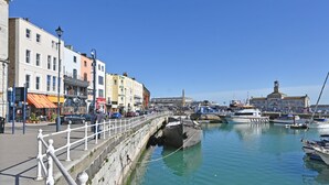 Une promenade en bord de mer, avec un mur de pierre, une rangée de bâtiments aux couleurs vives et un port de plaisance rempli de bateaux.
