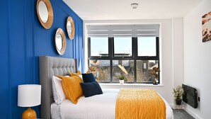 Une chambre moderne avec un grand lit, des murs bleus et une fenêtre donnant sur la ville.