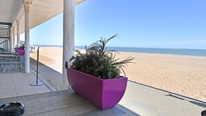 Une vue sur la plage avec un pot de fleurs violet sur une terrasse en bois.