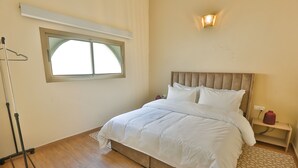 Quarto com cama, mesa de cabeceira, luminária, janela e abajur.