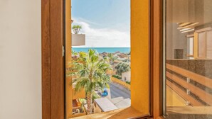 Un balcón con vista al mar, palmeras y una calle con coches.