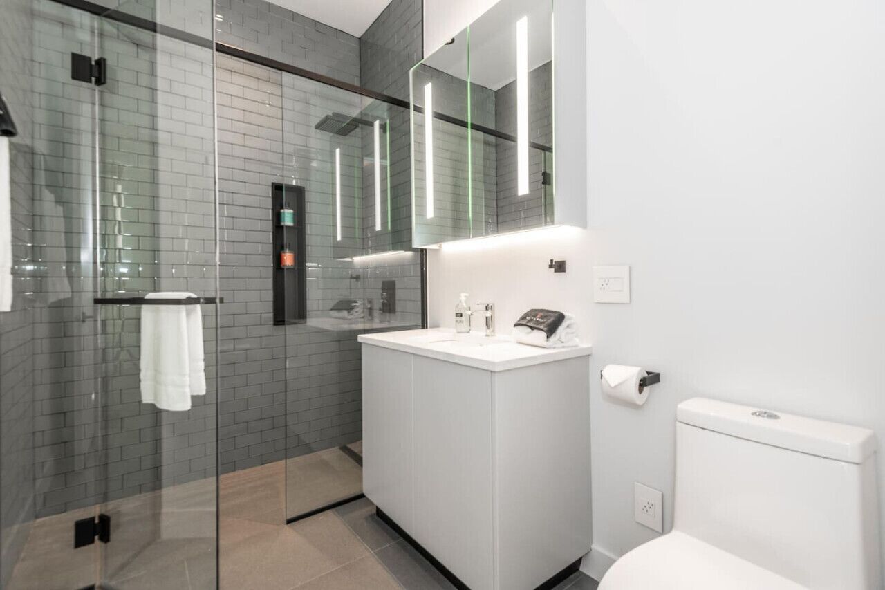 A modern bathroom with a glass shower enclosure, a white sink, and a toilet.