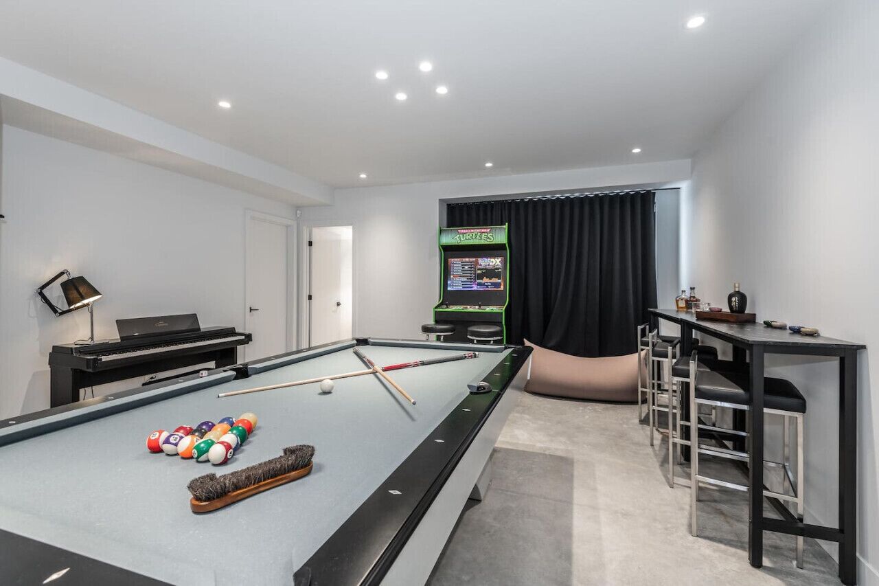 A pool table with balls, a piano, and a gaming machine in a room with a black curtain and a bar area.