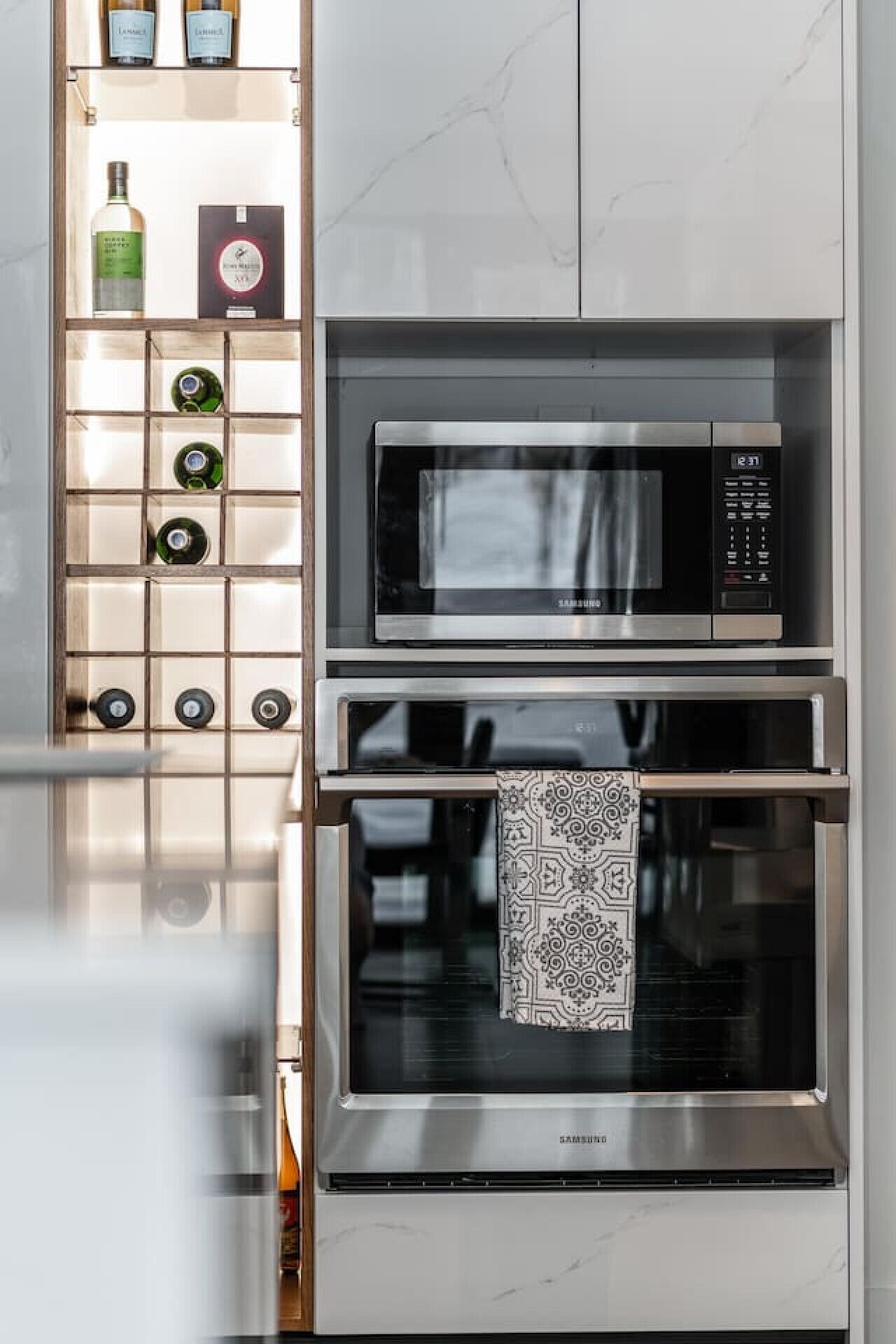 Une cuisine équipée d’un four à micro-ondes et d’un four encastrés, d’un meuble à vin contenant des bouteilles, et d’un tissu à motifs suspendu à l’intérieur du four.