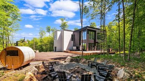 A modern cabin with a wooden sauna, outdoor seating, and a deck overlooking a forest. - Nordic Lodge Tremblant -5 Bdrs,Hot Tub,Pool Table (La Conception)