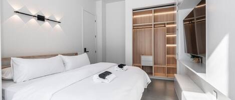 A modern hotel room with a large bed, a walk-in closet, and a built-in TV.