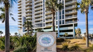 A sign for Emerald Dolphin at 850 Fort Pickensroad, featuring a dolphin logo and surrounded by palm trees and a building with multiple balconies.