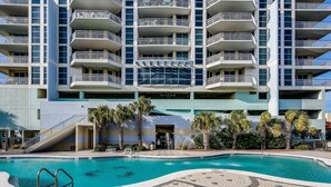 A modern hotel with a swimming pool, multiple balconies, and a staircase leading to the entrance.